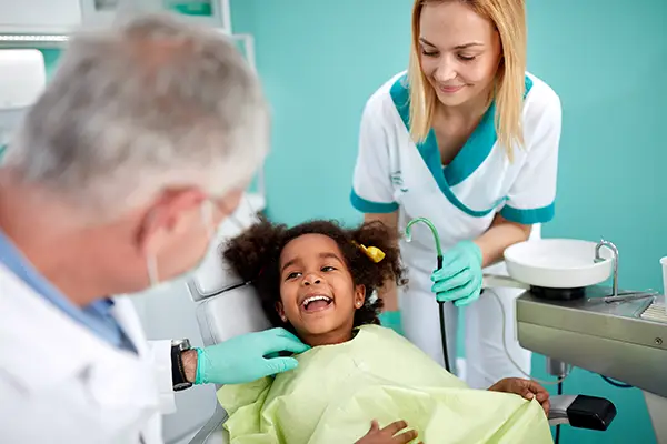 Young girl sitting in a dental chair and smiling at her dentist and dental assistant