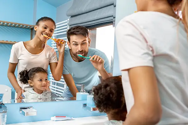 A diverse family brushing their teeth together in the mirror, demonstrating the power of family dentistry.