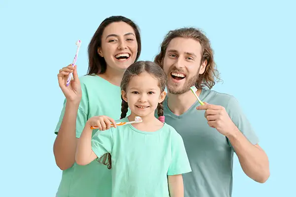 A little girl with her parents smiling and brushing their teeth together